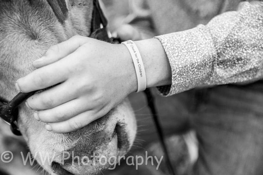 A person gently holds a cow’s face, wearing a wristband that reads “Cowgirl for my Guardian.” The image is in black and white and watermarked with “WW Photography.”.