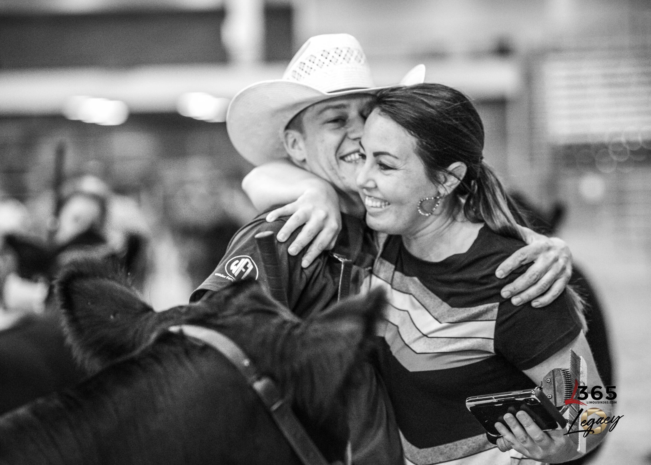 A young woman with wavy blonde hair smiles at the camera. She is wearing a black jacket over a red collared shirt, and stands in front of a wooden background.
