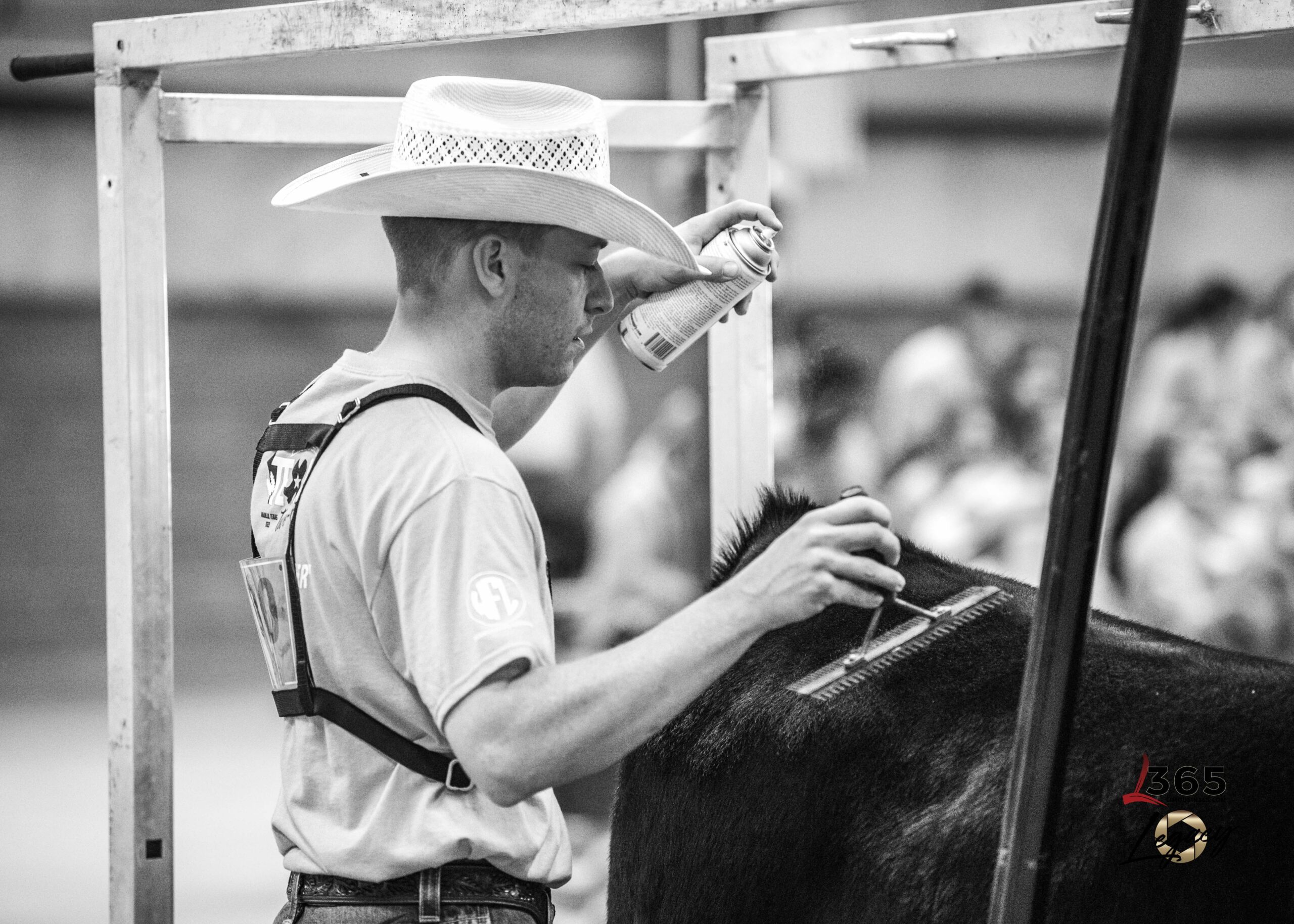 A young man wearing glasses, a black cowboy hat, a red shirt, and a dark blazer stands in front of wooden steps. He has a name badge pinned to his jacket.