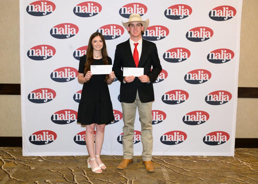 Two young people stand side by side, smiling and holding envelopes in front of a backdrop with repeated nalja logos. The girl wears a black dress and the boy wears a suit with a red tie and cowboy hat.
