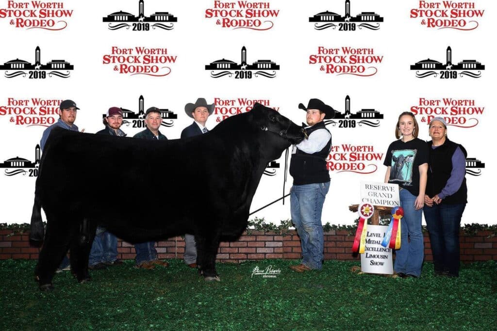 A group of people poses with a large black cow at the Fort Worth Stock Show & Rodeo. One person holds the cow’s lead, while another holds a banner that reads Reserve Grand Champion.