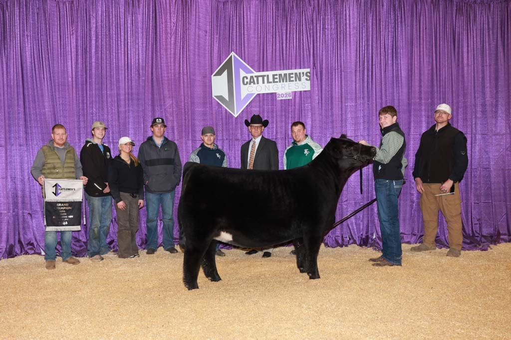 A group of people pose with a black cow in front of a purple curtain at the 2021 Cattlemen's Congress. One person holds a banner.
