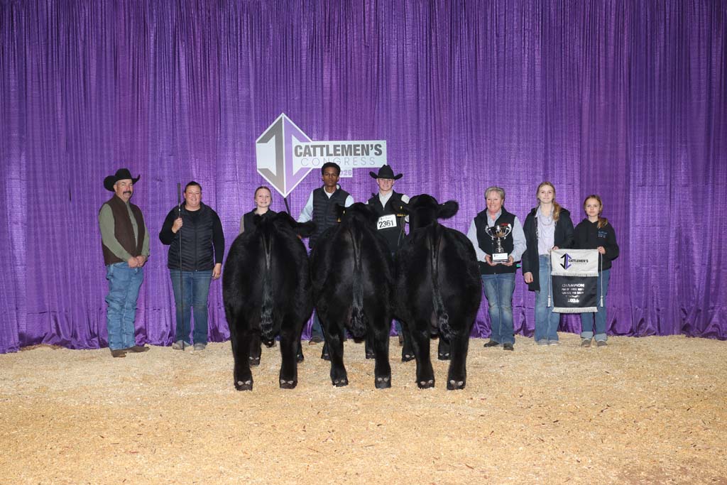A group of people stand behind three black cattle in front of a purple curtain with a "Cattlemen's Congress" sign. Some hold awards and a banner.